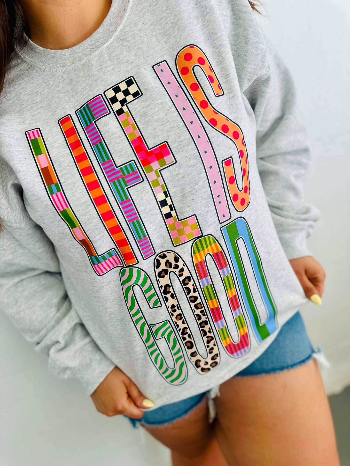 Gray sweatshirt with colorful text design worn by a person.